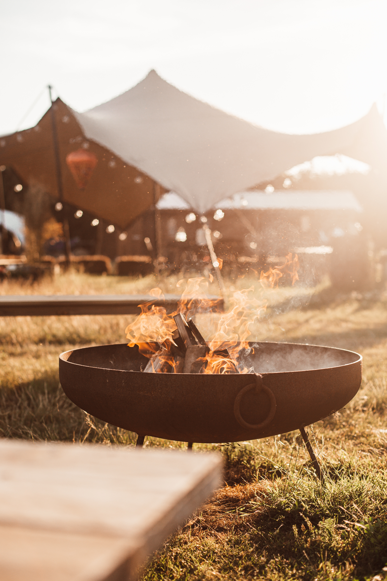 Fire pit crackling in front of the stretch tent at golden hour